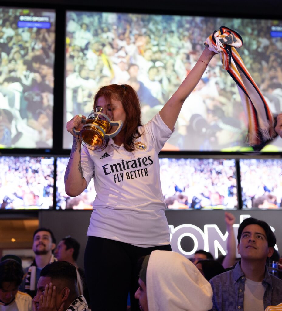 Girl Drinking Beer In Soccer Gear In front of Soccer on the big screen