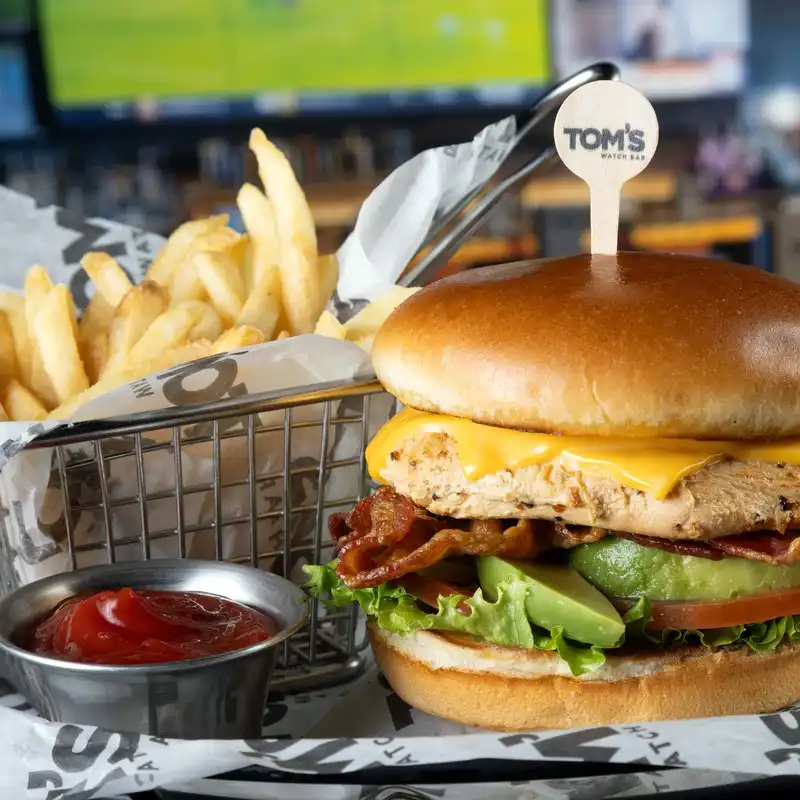 California Chicken Club with Fries Grilled chicken club sandwich with bacon, avocado, and cheese served with fries at Tom's Watch Bar