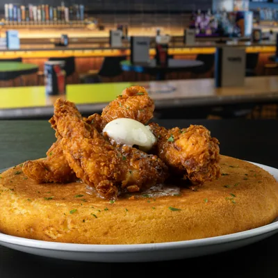Chicken Tenders and Cornbread Pancake at Tom’s Watch Bar Crispy chicken tenders topped with whipped butter on a golden cornbread pancake, served on a white plate at Tom's Watch Bar